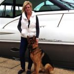 A woman and her protection dog posing next to a boat